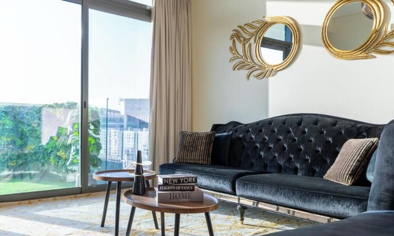 Een moderne woonkamer met een zwarte bank, een ronde salontafel en een stadsgezicht door grote ramen.