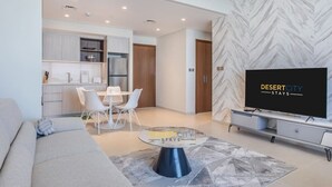 Ein modernes Wohnzimmer mit einer Couch, einem Esstisch mit Stühlen, einem Fernseher und einer Küche im Hintergrund.