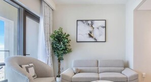 A modern living room with a sofa, a chair, a potted plant, and a framed artwork on the wall. - Vida Residence 1BR | Creek Beach Access included (Dubai)