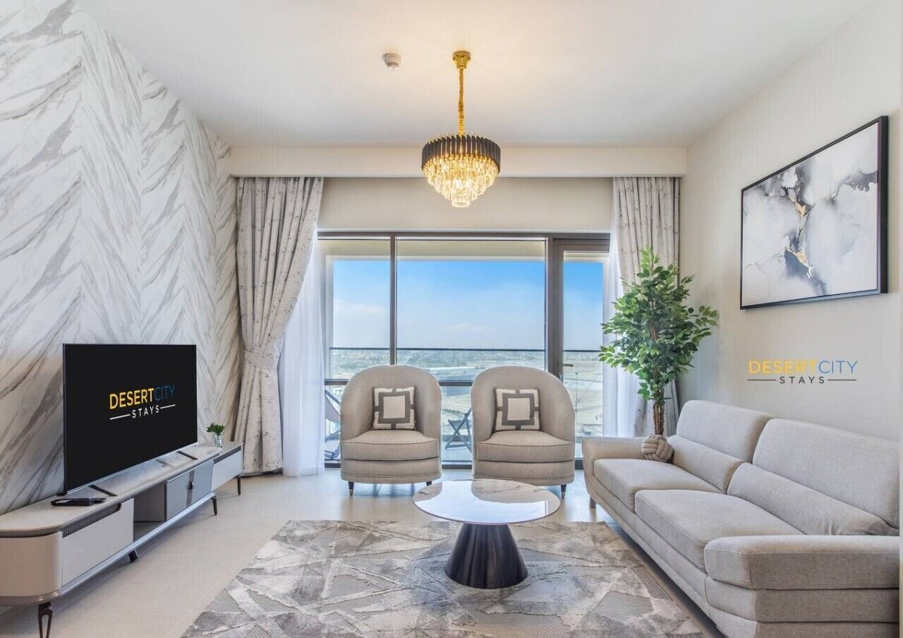 A modern living room with a TV, two armchairs, a sofa, a chandelier, and a large window with a view.