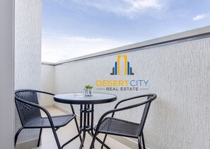 A small outdoor seating area with a table and two chairs, a logo for Desert City Real Estate, and a textured wall. - Restaurants nearby | Supermarket 5 mins away. (Dubai)