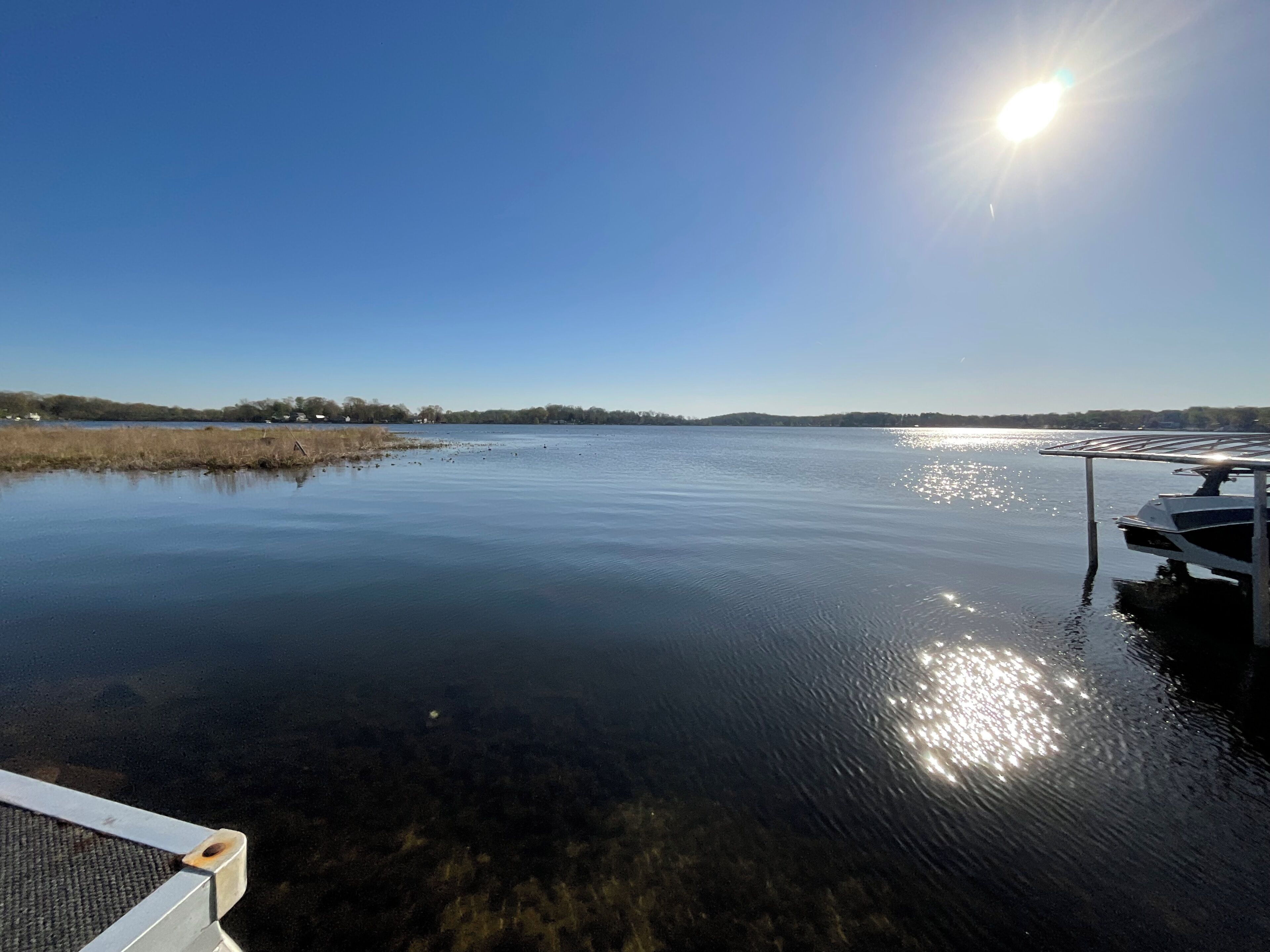 En stilla sjö med en brygga som sträcker sig ut i vattnet, omgiven av träd och en klar himmel.