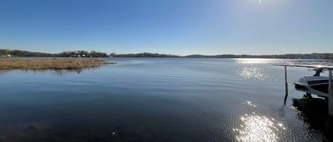 En stilla sjö med en brygga som sträcker sig ut i vattnet, omgiven av träd och en klar himmel.