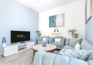 Un salon moderne avec un téléviseur à écran plat, un ensemble de canapés gris, une table basse et un tableau accroché au mur.