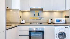 A modern kitchen with a microwave, toaster, gas stove, oven, and washing machine. - Modern 2BR Sobha Hartland | Pool & Fast WiFi (Dubai)