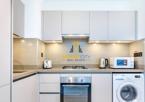 A modern kitchen with a microwave, toaster, gas stove, oven, and washing machine. - Modern 2BR Sobha Hartland | Pool & Fast WiFi (Dubai)