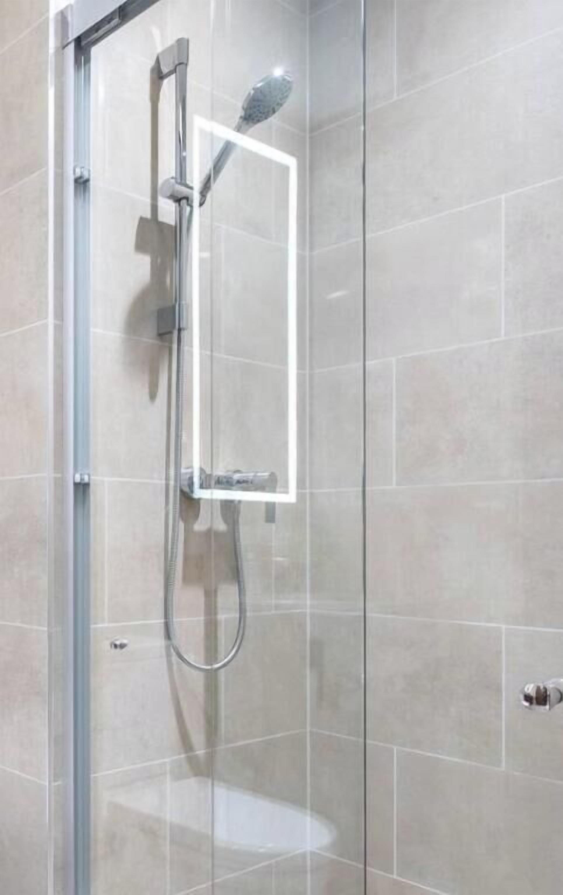Un espace douche clos par des parois de verre, doté d’un pommeau de douche à main et d’un panneau de commande fixé au mur.