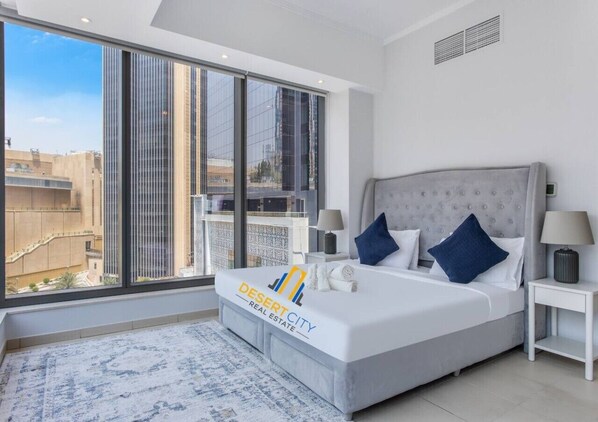 A modern bedroom with a large bed, two bedside tables, a window with a city view, and a logo on the bed. - Close to Marina Mall/ Carrefour below the building (Dubai)