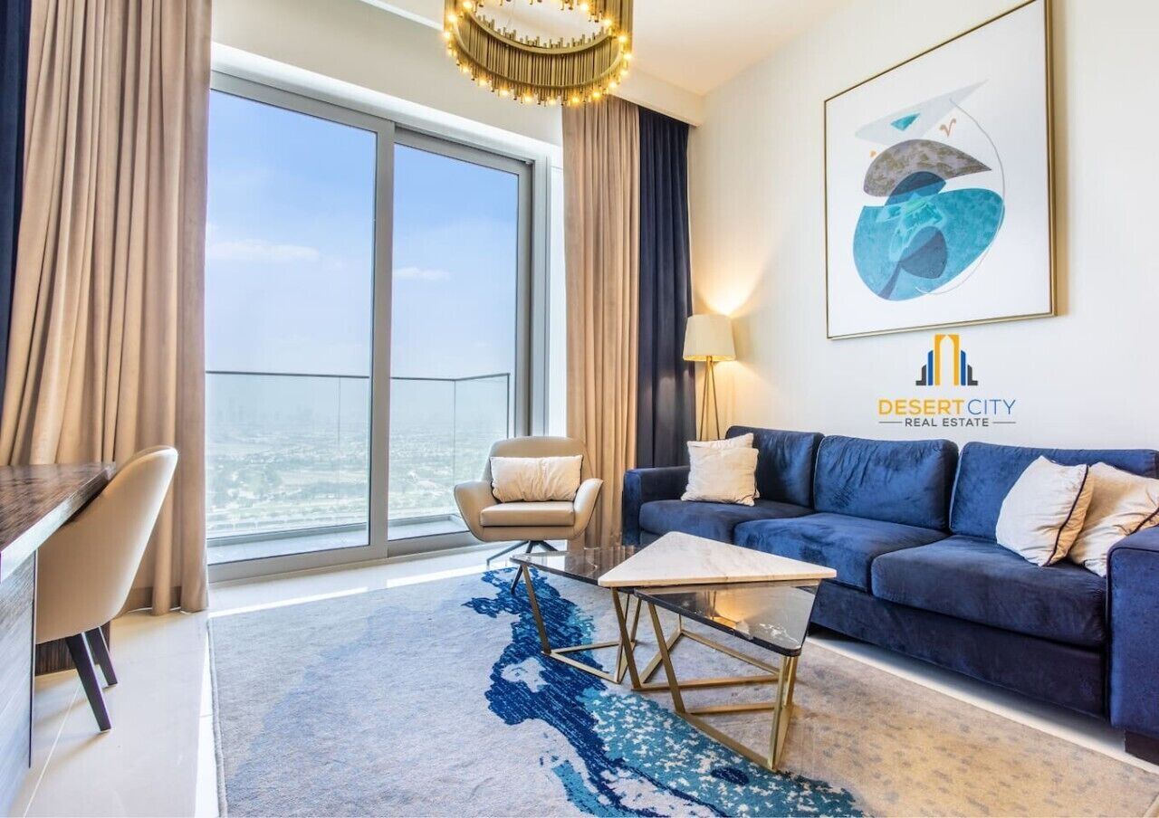 Una habitación de hotel moderna con un balcón grande, un sofá azul, una mesita pequeña y vistas a la ciudad.