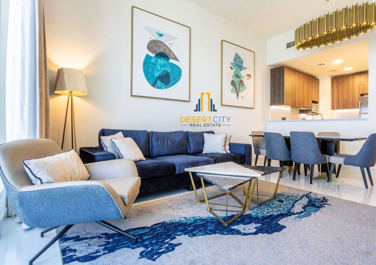 Een moderne woonkamer met een bank, fauteuil en salontafel, een eethoek met stoelen, en een keuken op de achtergrond.