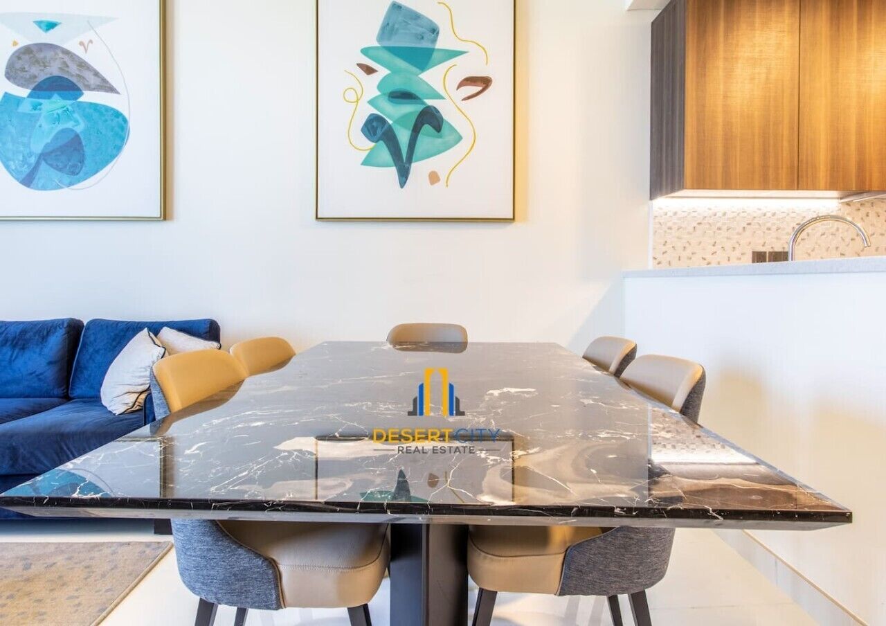 A modern living room with a glass-top dining table, a blue sofa, and abstract art on the wall.