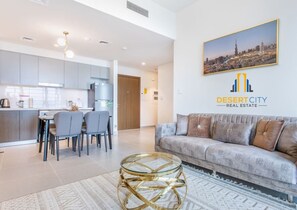 A modern living room with a sofa, a dining area with chairs, a kitchen in the background, and a cityscape view. - Supermarket`s Nearby| Restaurants around the tower (Dubai)