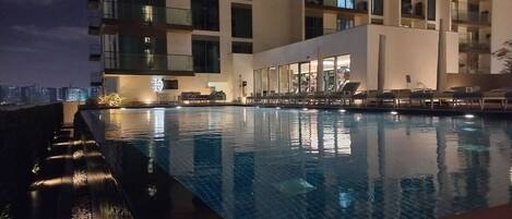 Vue nocturne d’une piscine d’hôtel au design moderne, entourée d’un immeuble à plusieurs étages doté de balcons.