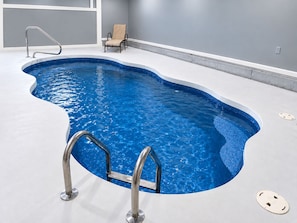 A swimming pool with a curved edge, a metal ladder, and a chair.