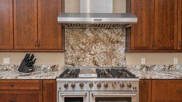 A kitchen with wooden cabinets, a stainless steel range hood, a gas stove, and a double oven.