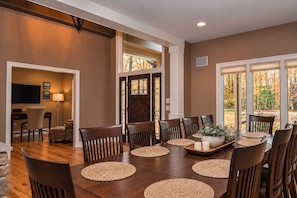 A dining area with a large wooden table, multiple chairs, and a television in the background.