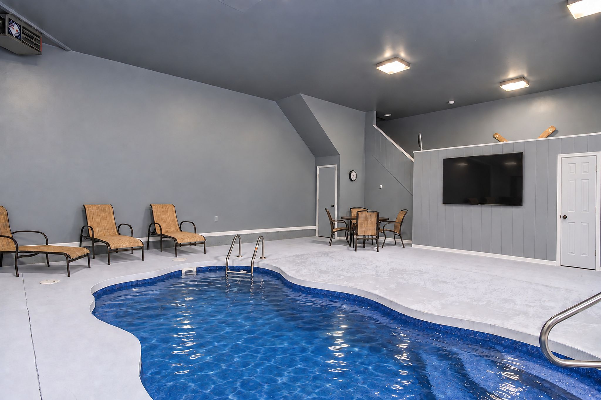 A swimming pool with a sloped ceiling and a flat floor, surrounded by lounge chairs and a table.