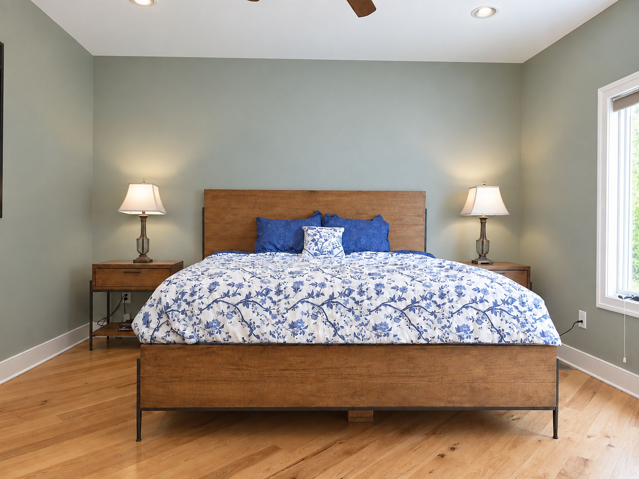 A bedroom with a wooden bed, two bedside tables with lamps, a window, and a ceiling fan.