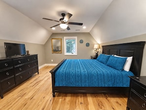 A bedroom with a bed, dresser, ceiling fan, and a window.