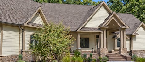 A two-story house with a stone foundation, a covered porch, and a well-maintained front yard with various plants.