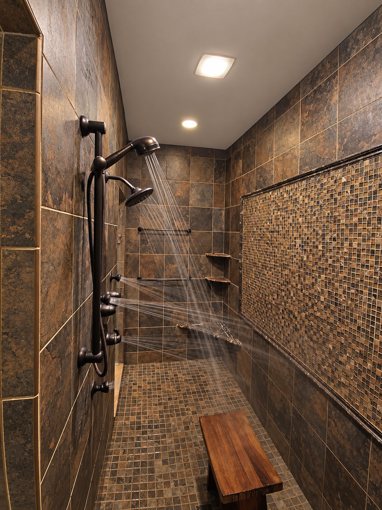 Une douche moderne dotée de plusieurs pommeaux, d’un banc et d’un mur décoratif recouvert de carreaux.