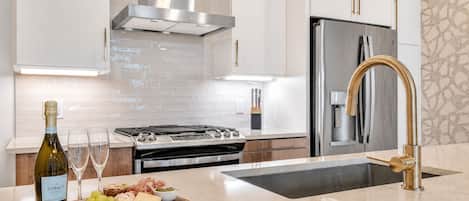 A modern kitchen with stainless steel appliances, a marble countertop, and a wine bottle.