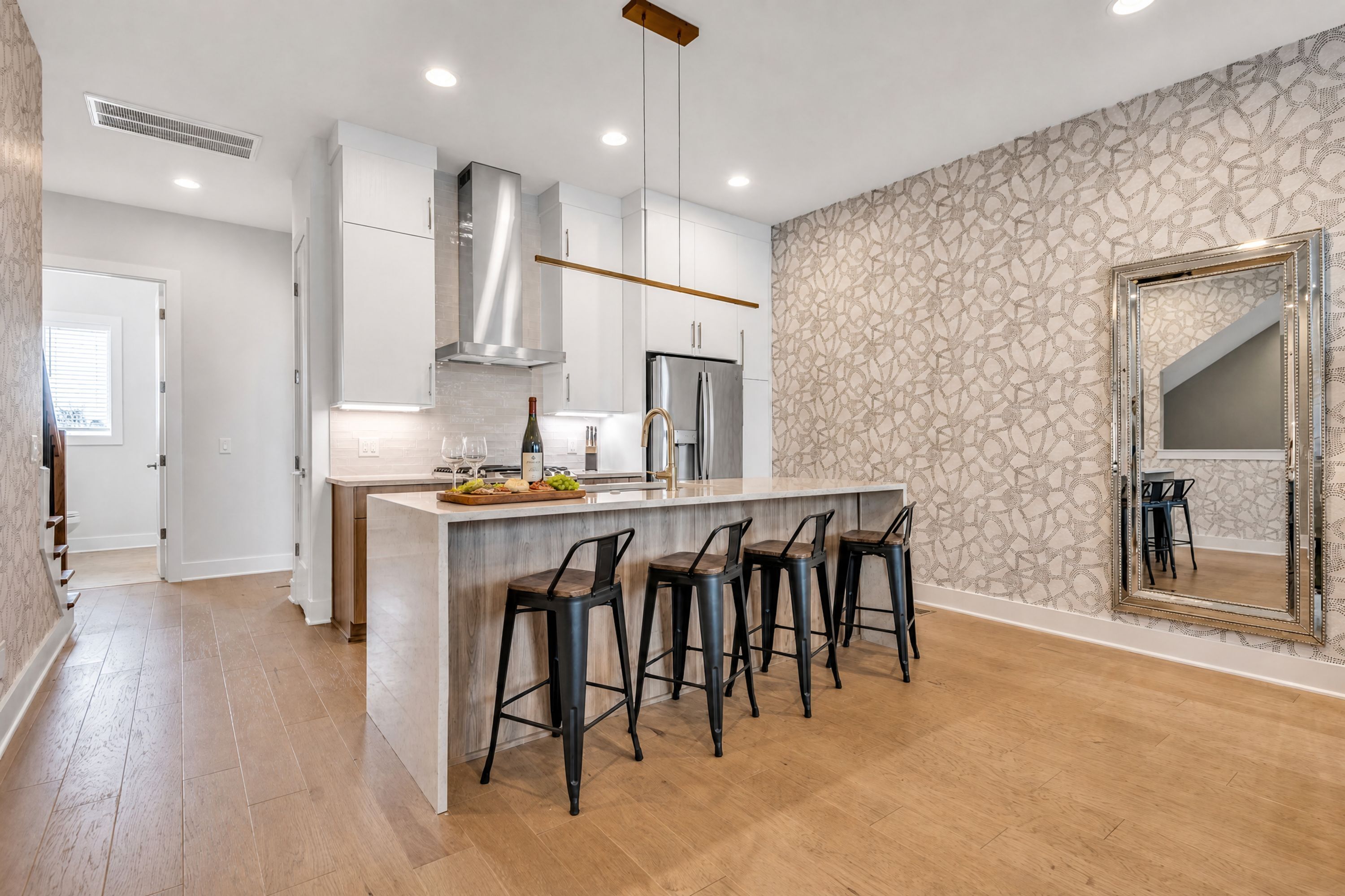 A modern kitchen with a central island, bar stools, and a patterned wallpaper.