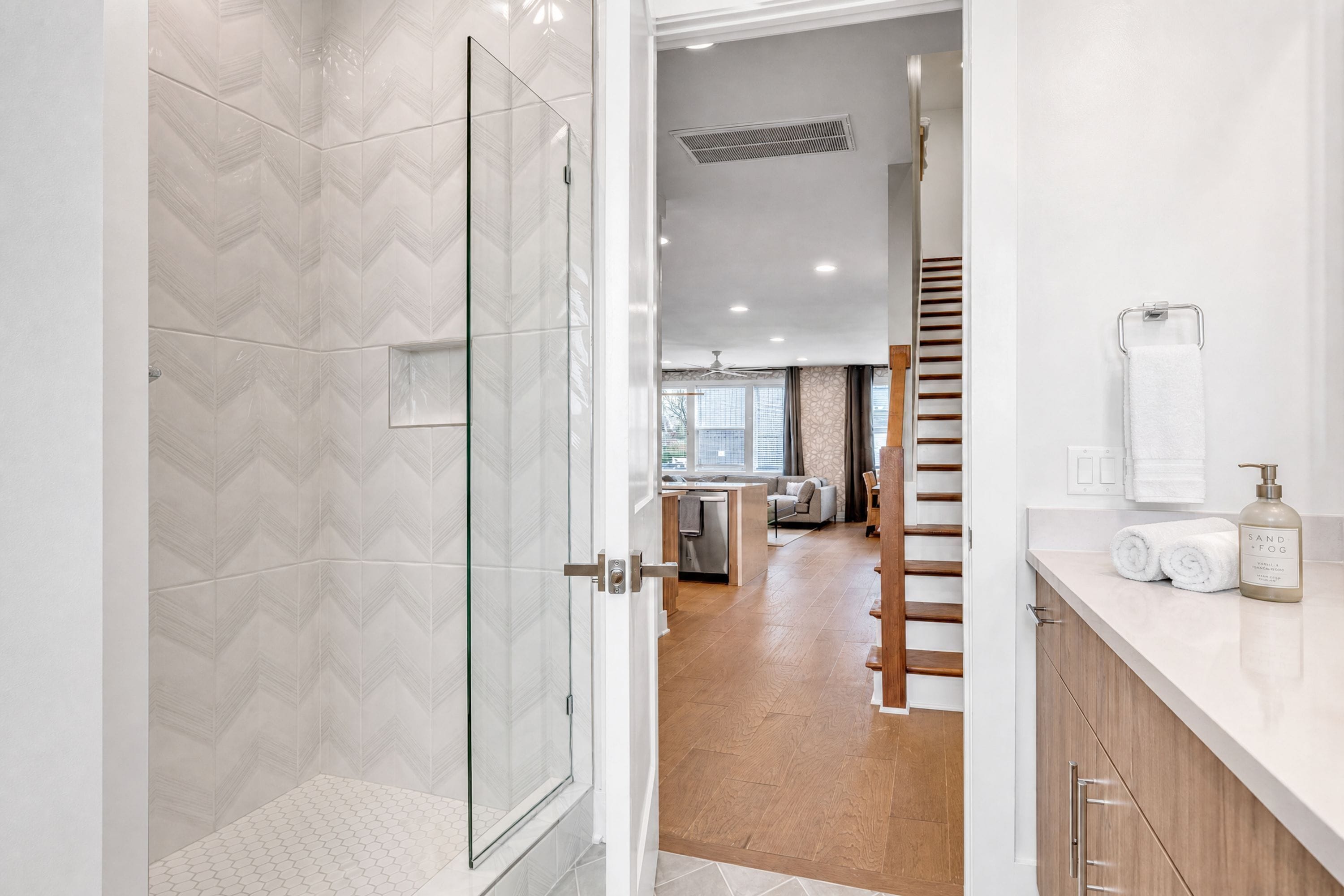 A modern bathroom with a glass shower door, a toilet, and a sink with a towel and soap dispenser.