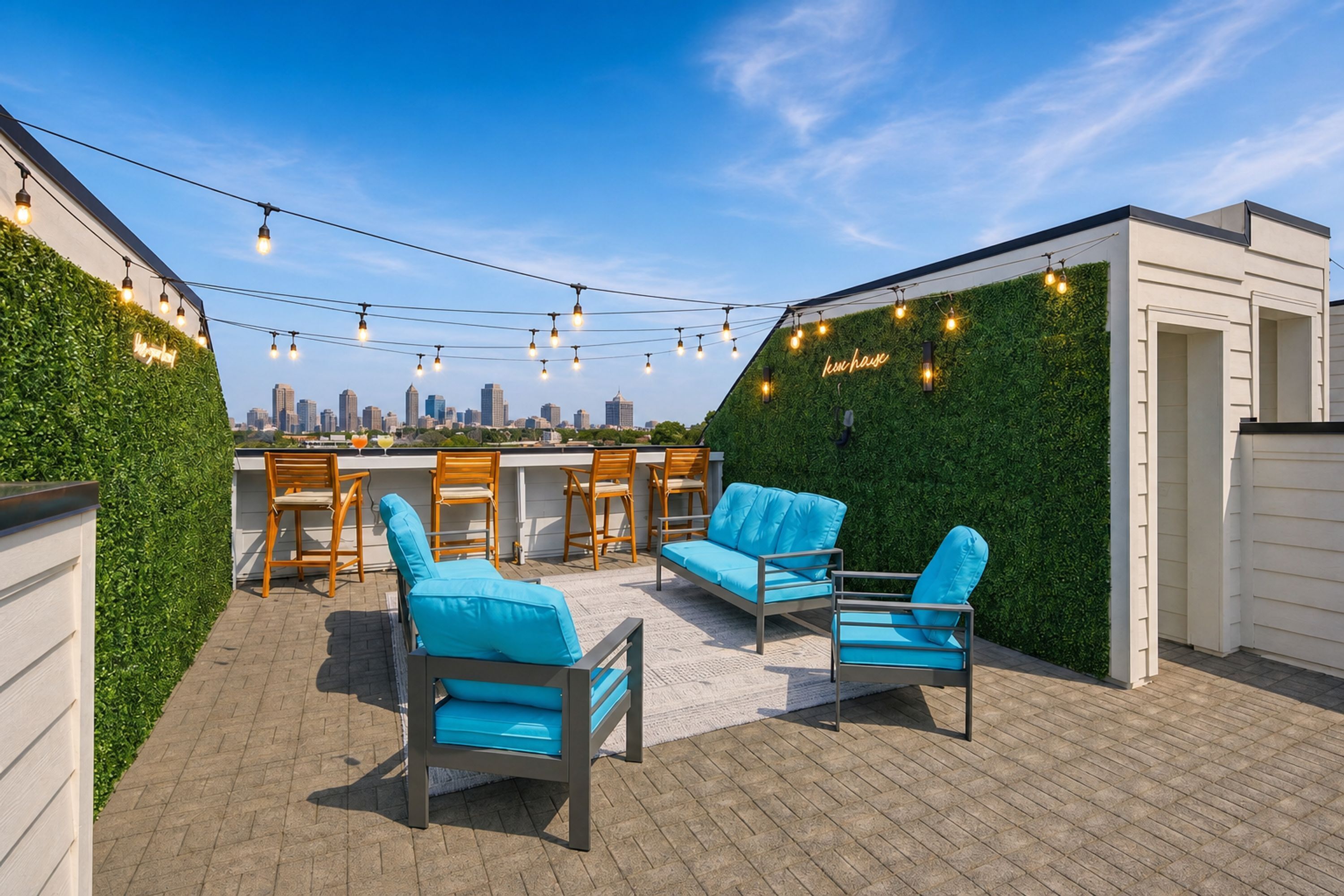 An outdoor seating area with chairs and a table, a green wall with a neon sign, and a city skyline in the background.