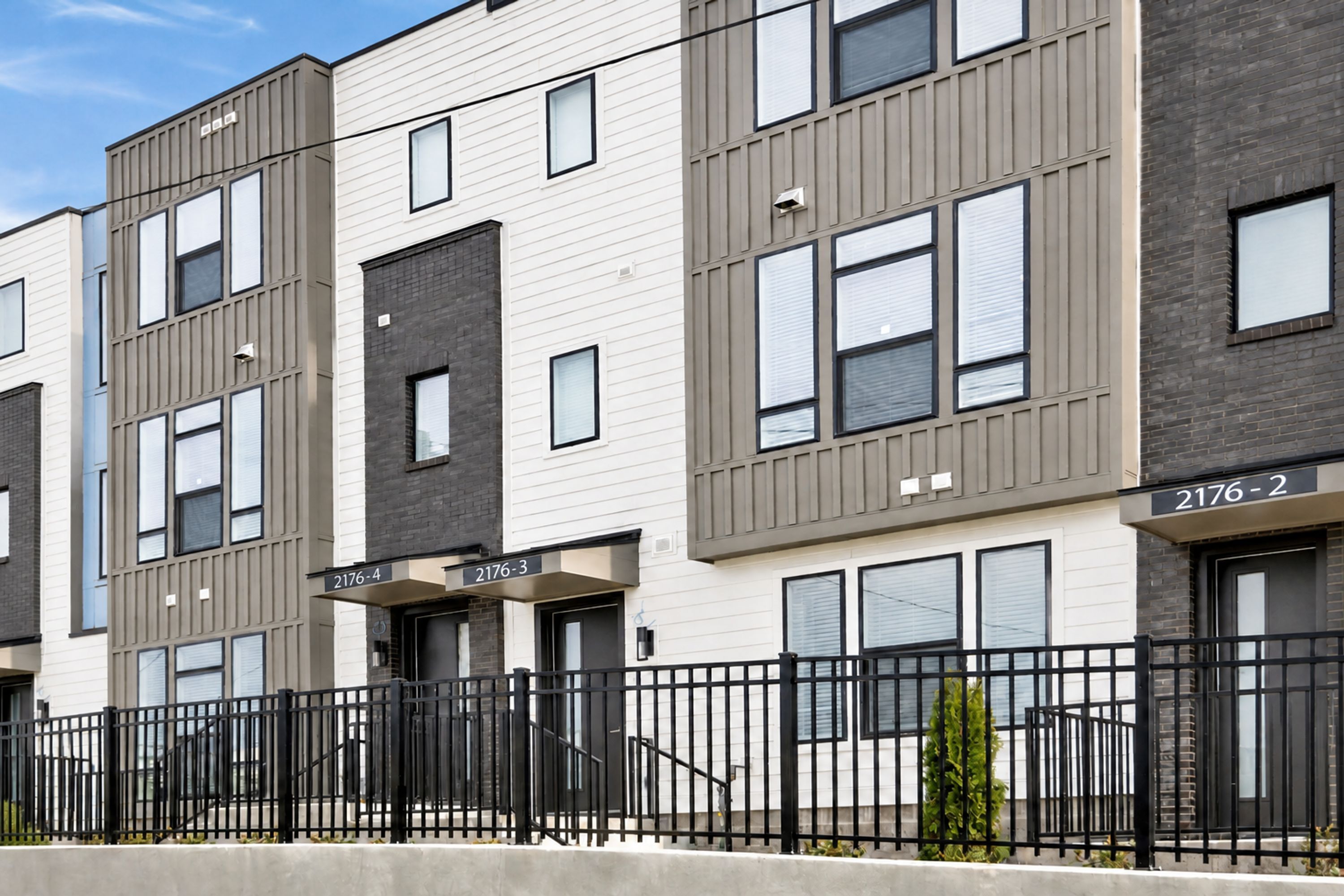 A modern multi-story residential building with numbered units, a black metal fence, and a clear sky.