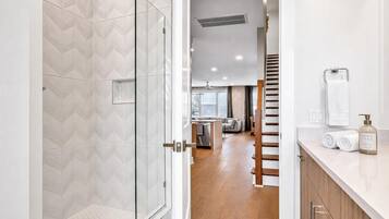 Un baño moderno con cabina de ducha de vidrio, inodoro y lavamanos con toalla y dispensador de jabón.