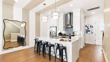 Una cocina moderna con una isla central, taburetes de bar, iluminación colgante y un espejo grande.