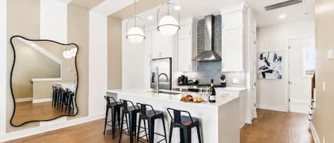 A modern kitchen with a central island, bar stools, pendant lighting, and a large mirror.