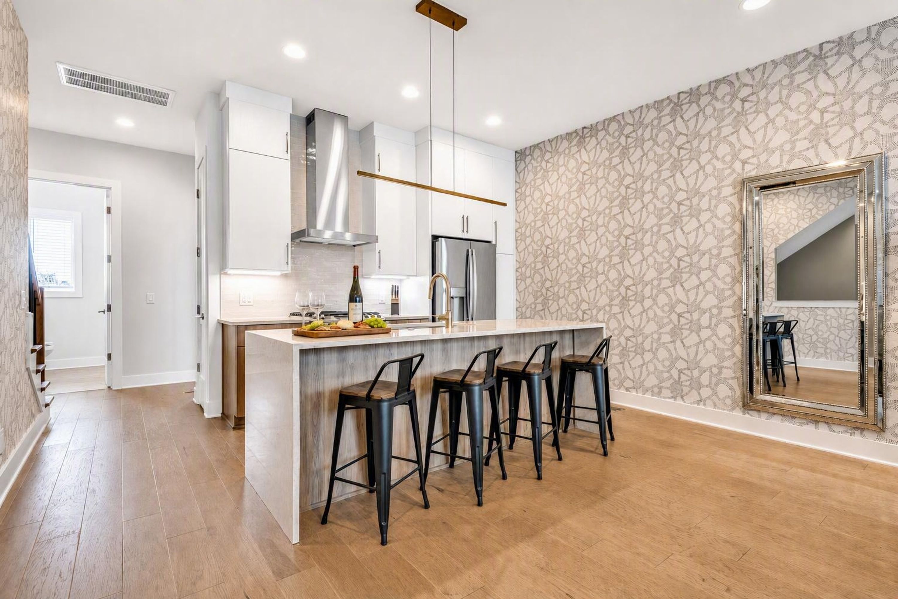 A modern kitchen with a central island, bar stools, and a large mirror.