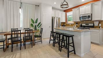 A modern kitchen with white cabinets, a stainless steel refrigerator, a microwave, and a large island with bar stools.