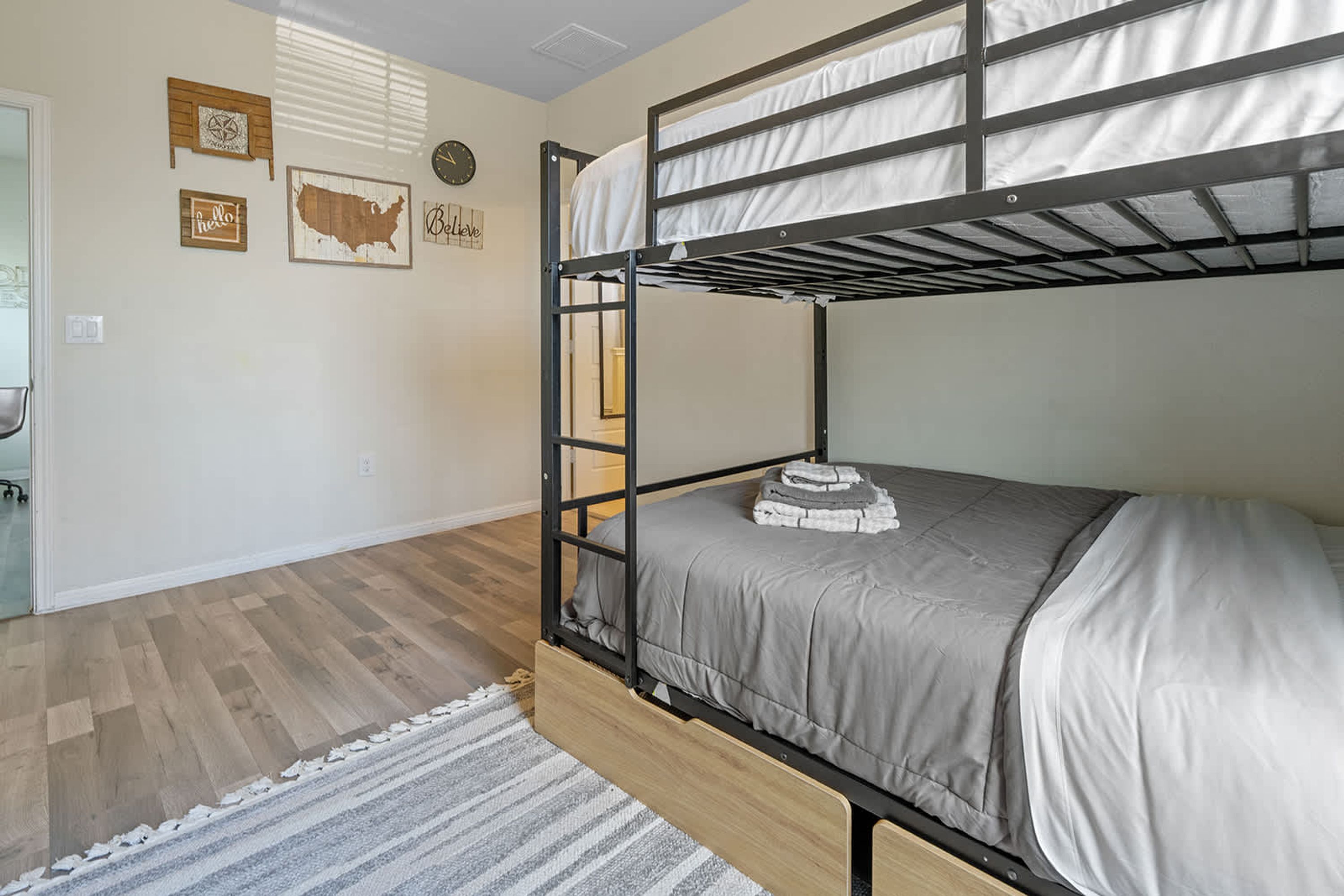 A bunk bed room with a wooden floor, a gray bedspread, and a white rug.