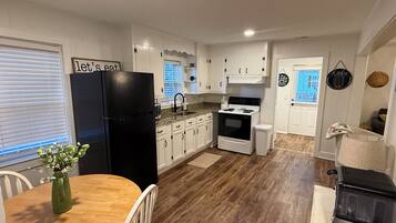 A kitchen with white cabinets, a black refrigerator, a wooden dining table with chairs, and a black stove.