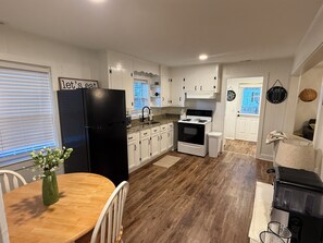 A kitchen with white cabinets, a black refrigerator, a wooden dining table with chairs, and a black stove.