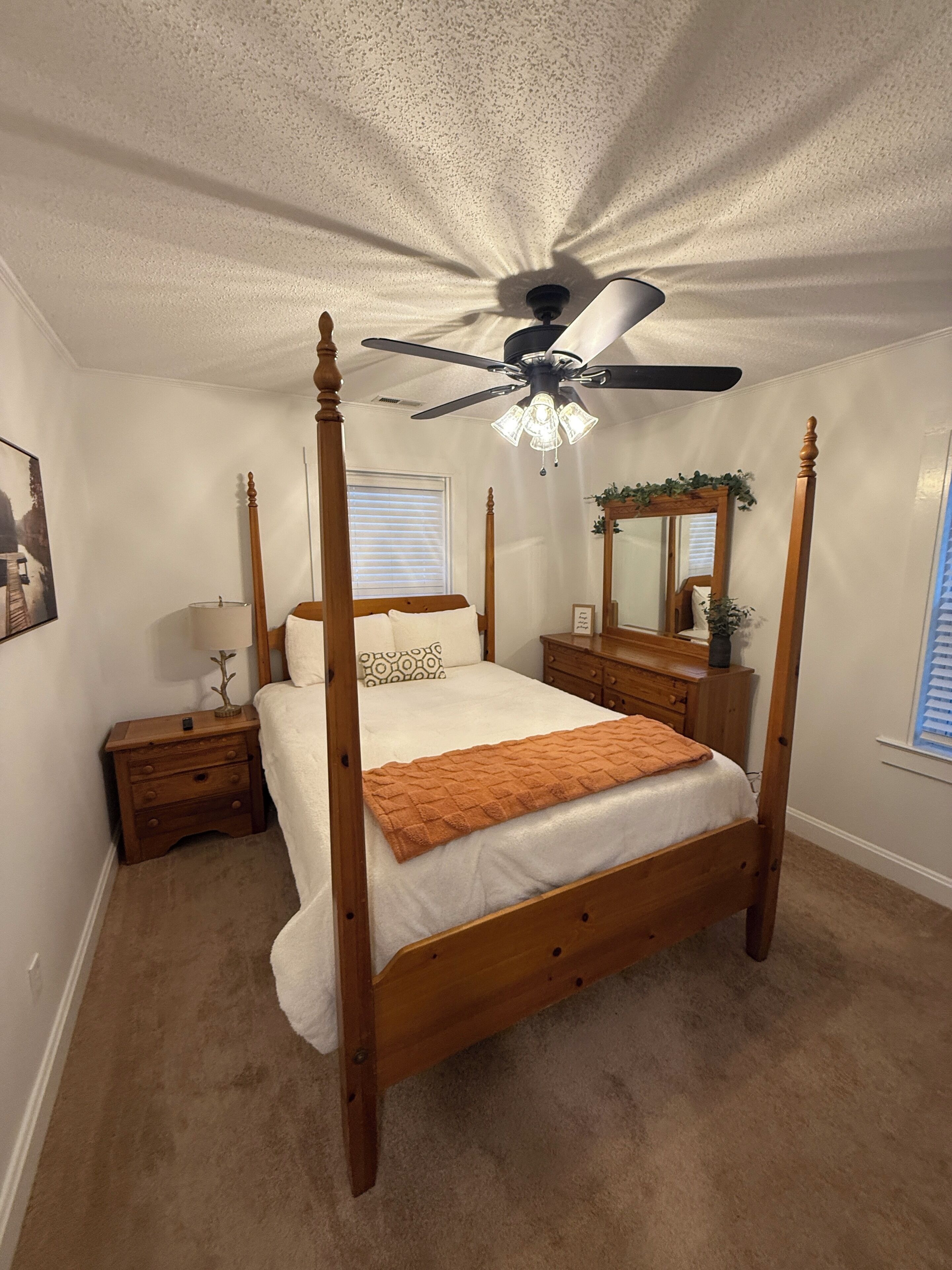 A four-poster bed with a wooden frame, a ceiling fan, and a nightstand with a lamp.