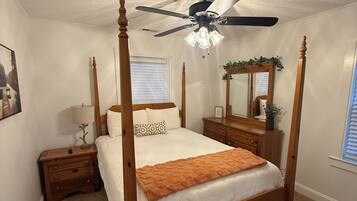 A four-poster bed with a wooden frame, a ceiling fan, and a nightstand with a lamp.