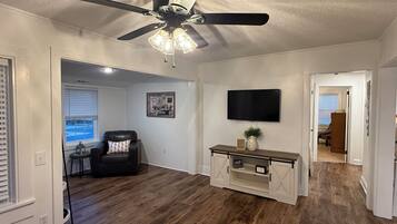 A living room with a ceiling fan, a flat-screen TV mounted on the wall, and a wooden floor.