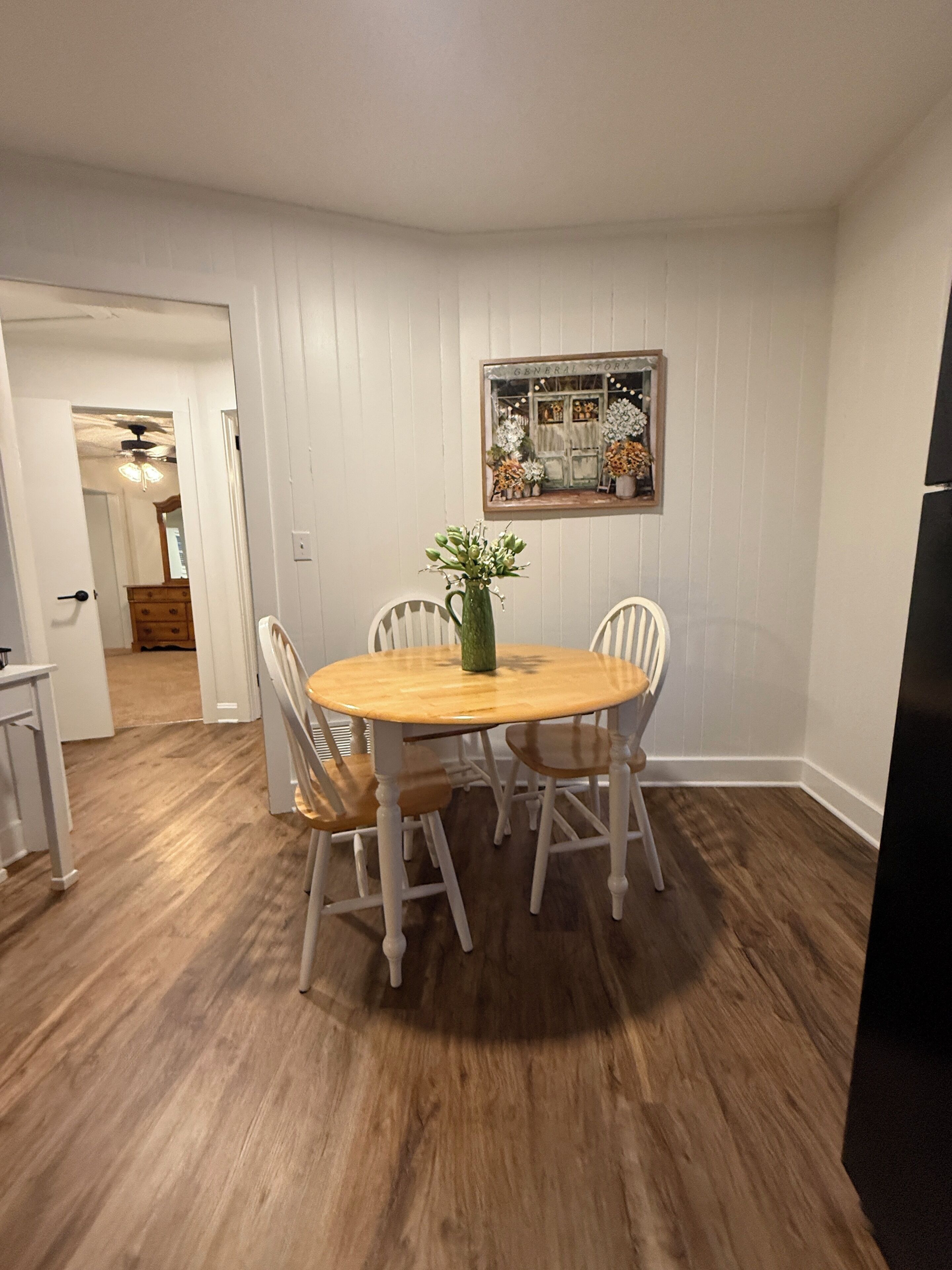 A dining area with a round wooden table surrounded by four chairs, a vase with flowers, and a mirror on the wall.
