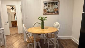 A dining area with a round wooden table surrounded by four chairs, a vase with flowers, and a mirror on the wall.