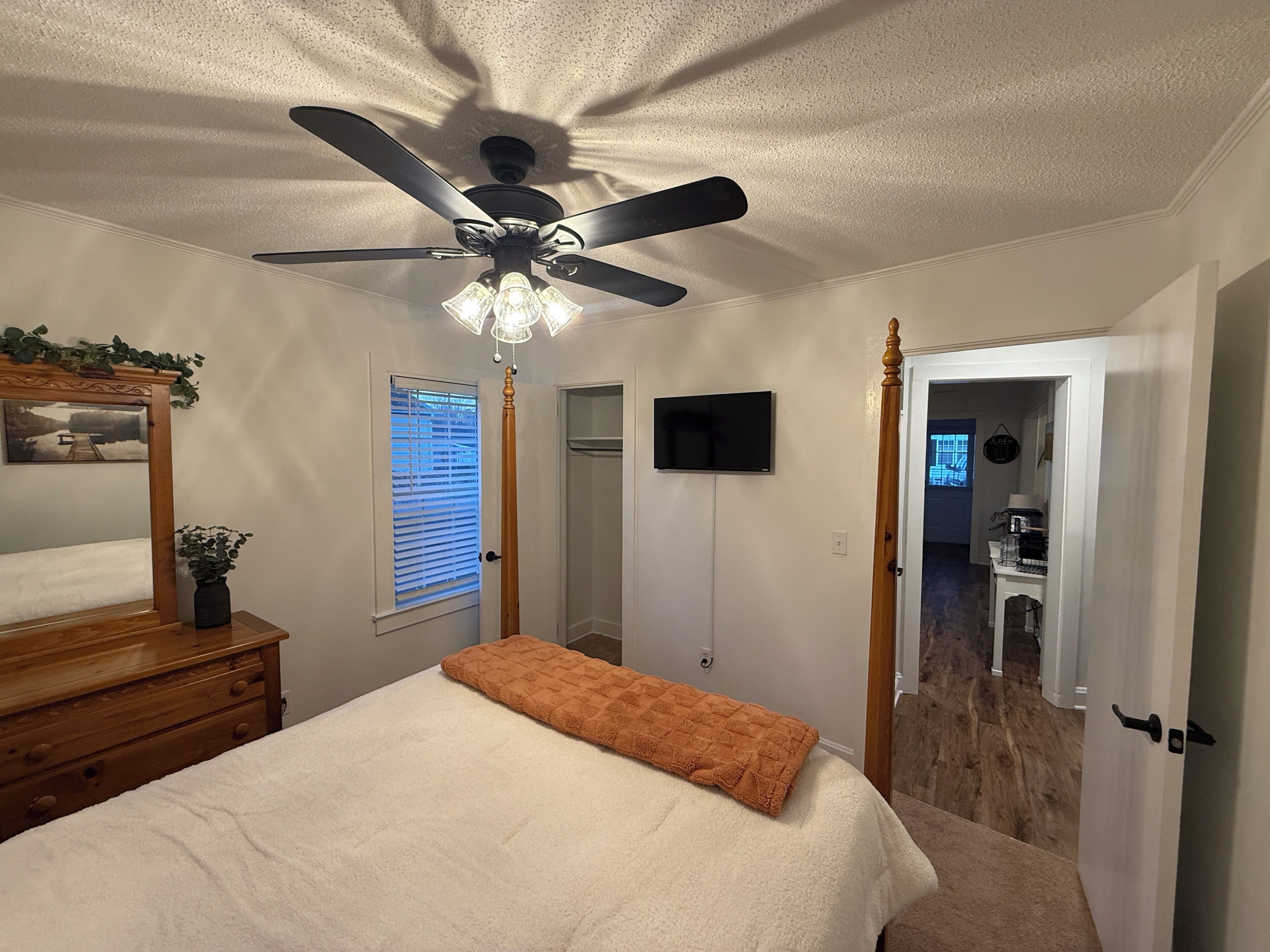 A bedroom with a bed, a ceiling fan, a TV, and a door leading to a bathroom.
