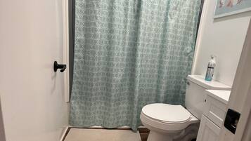 A bathroom with a shower curtain, toilet, and a small rug.