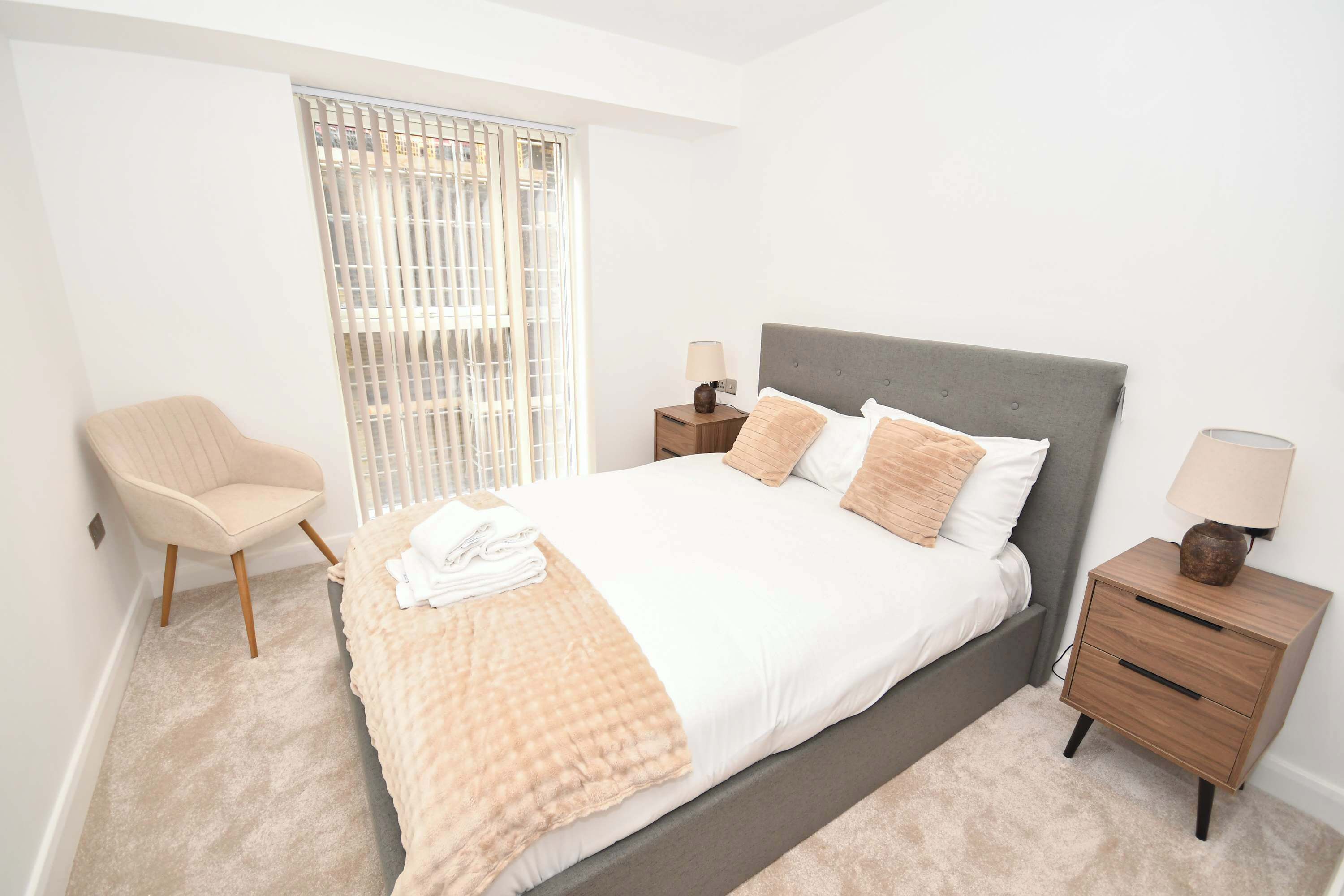 Een slaapkamer met een bed, een stoel, nachtkastjes en een raam met zonwering.