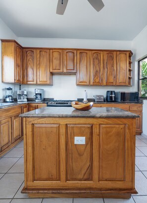 Una cocina con armarios de madera, encimera de granito y diversos electrodomésticos, incluyendo una cafetera y un microondas.