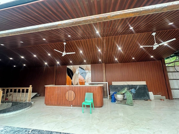 A reception area with a wooden reception desk, a green chair, and a ceiling fan. - Stillwood Resort Mussoorie (Mussorie Range)