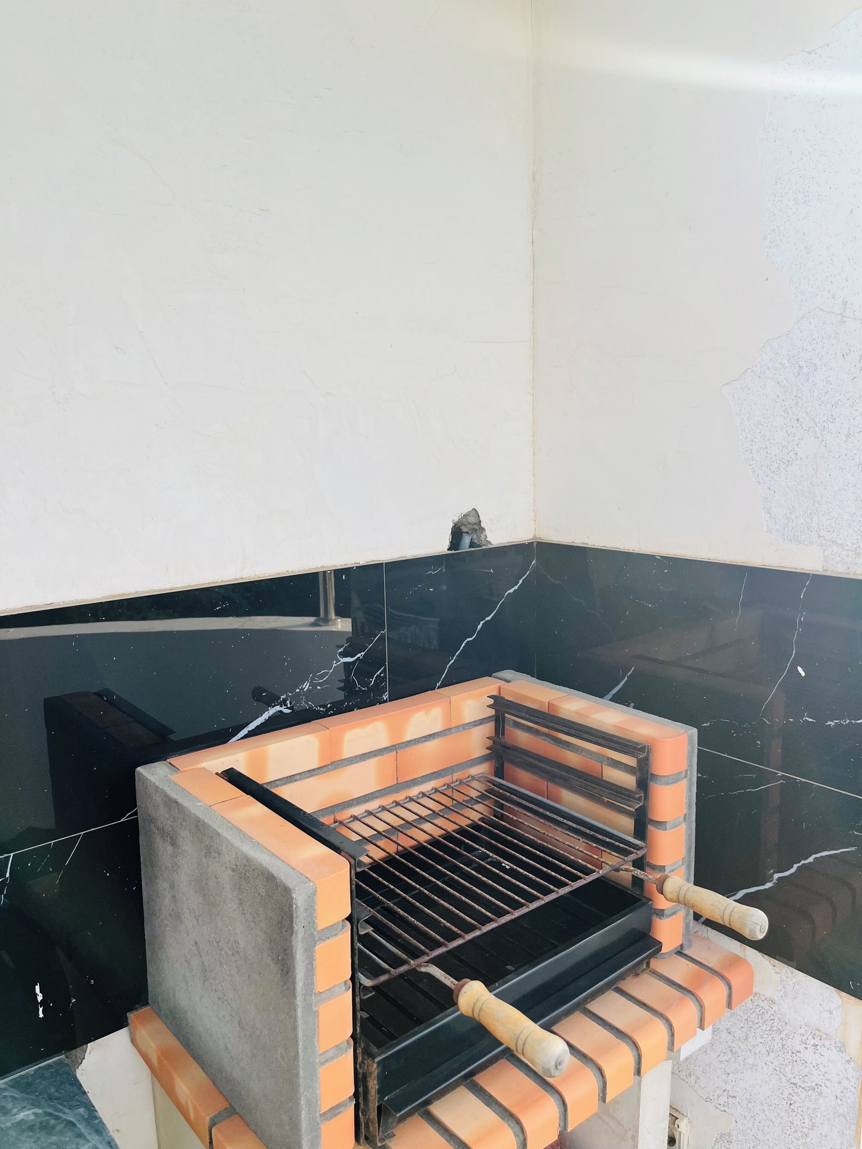 A brick-built outdoor grill with a metal grate, positioned against a wall with a black marble-like surface.