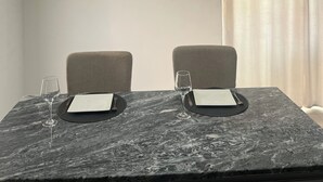 A dining area with a marble table, two chairs, a vase with flowers, and a ceiling light fixture.